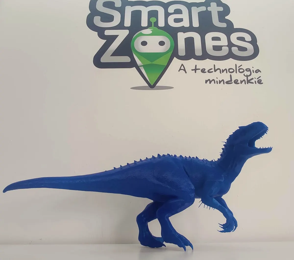 Kék, 3D nyomtatott dinoszaurusz a SmartZones.hu logó előtt