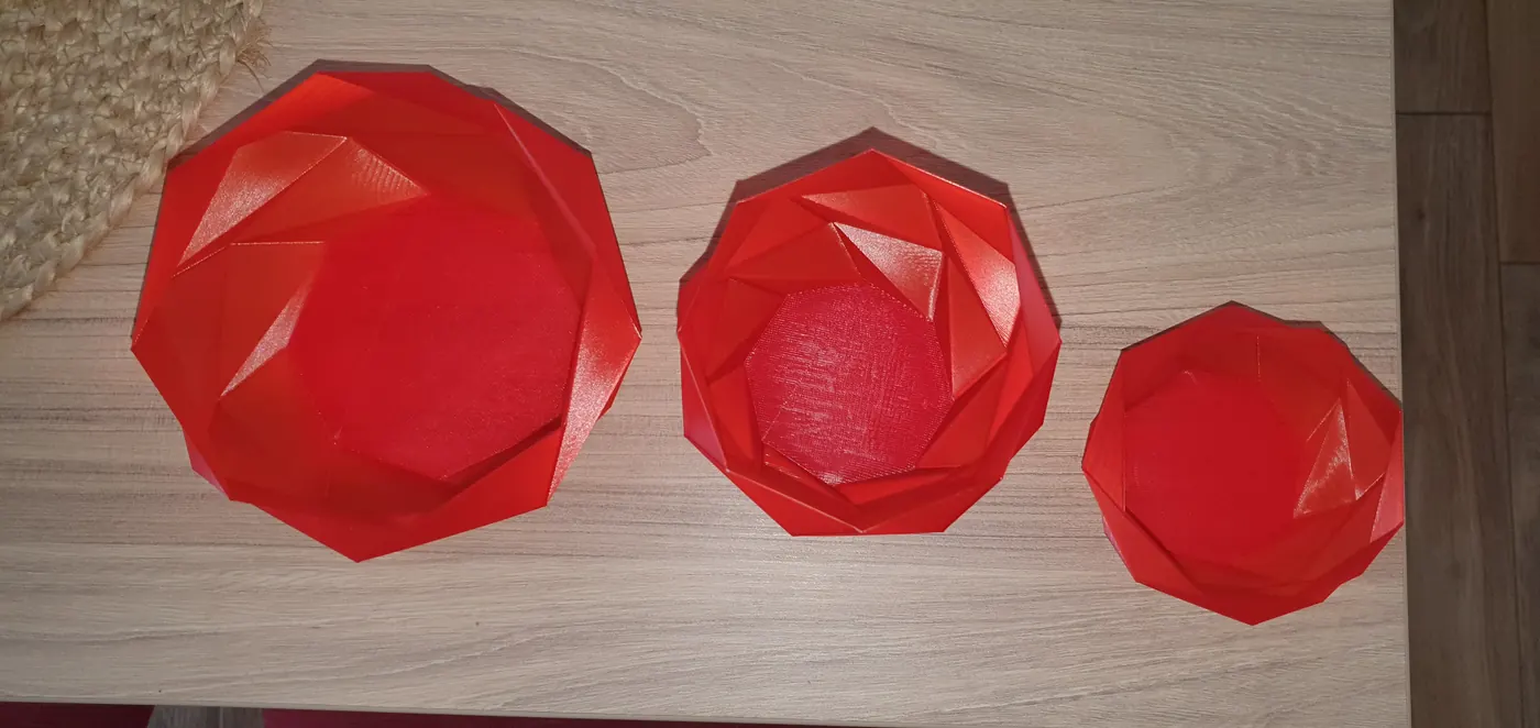 Három piros, geometrikus mintájú 3D nyomtatott tál egy asztalon