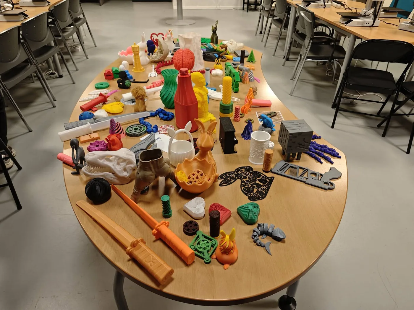 Hosszú asztal tele 3D nyomtatott tárgyakkal: dinoszaurusz-koponya, kardok, vázák, figurák, fogaskerekek